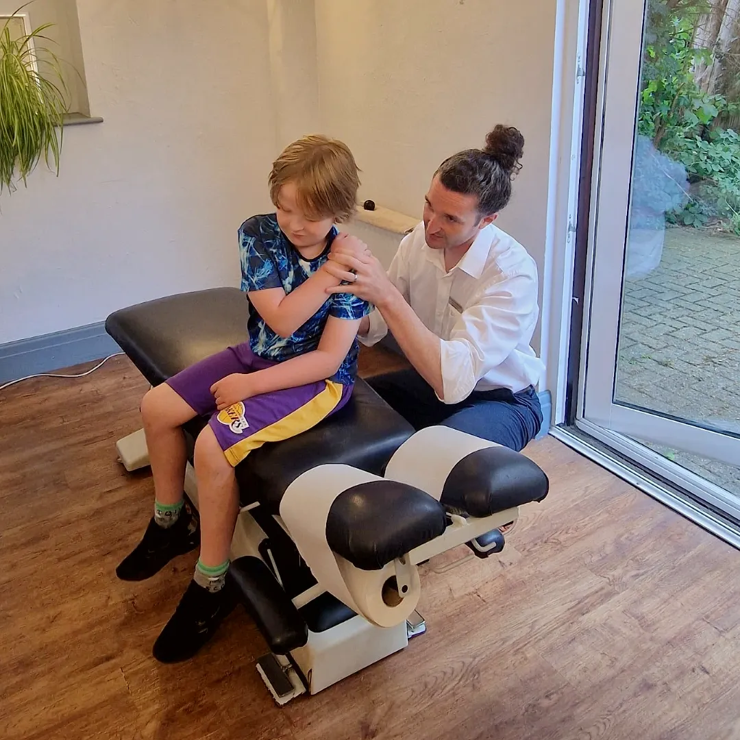 Chiropractor adjusting a child's shoulder in clinic.