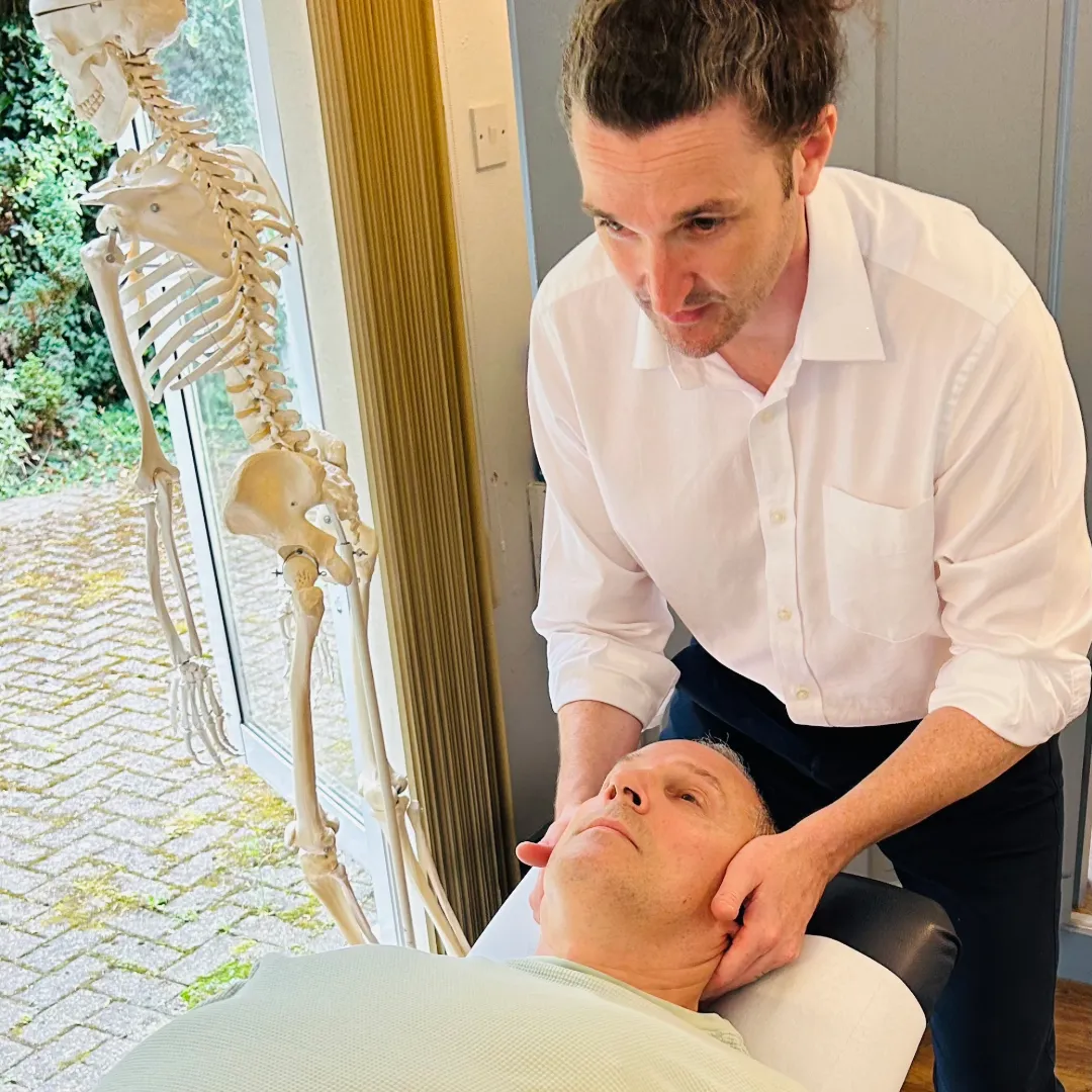 Chiropractor adjusting patient's neck with skeleton model nearby.